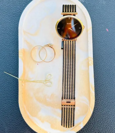 Montre dorée et bijoux sur plateau en marbre
